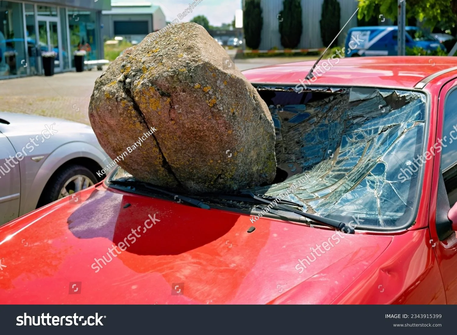 stock-photo-a-large-round-stone-rests-on-the-hood-of-a-red-car-with-a-shattered-windshield-23...webp